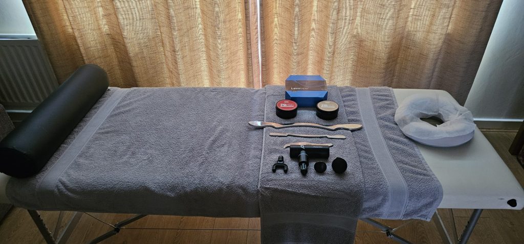 Treatment table set up with various sports massage tools, including IASTM instruments, cupping cups, creams, and a headrest, ready for a therapy session.